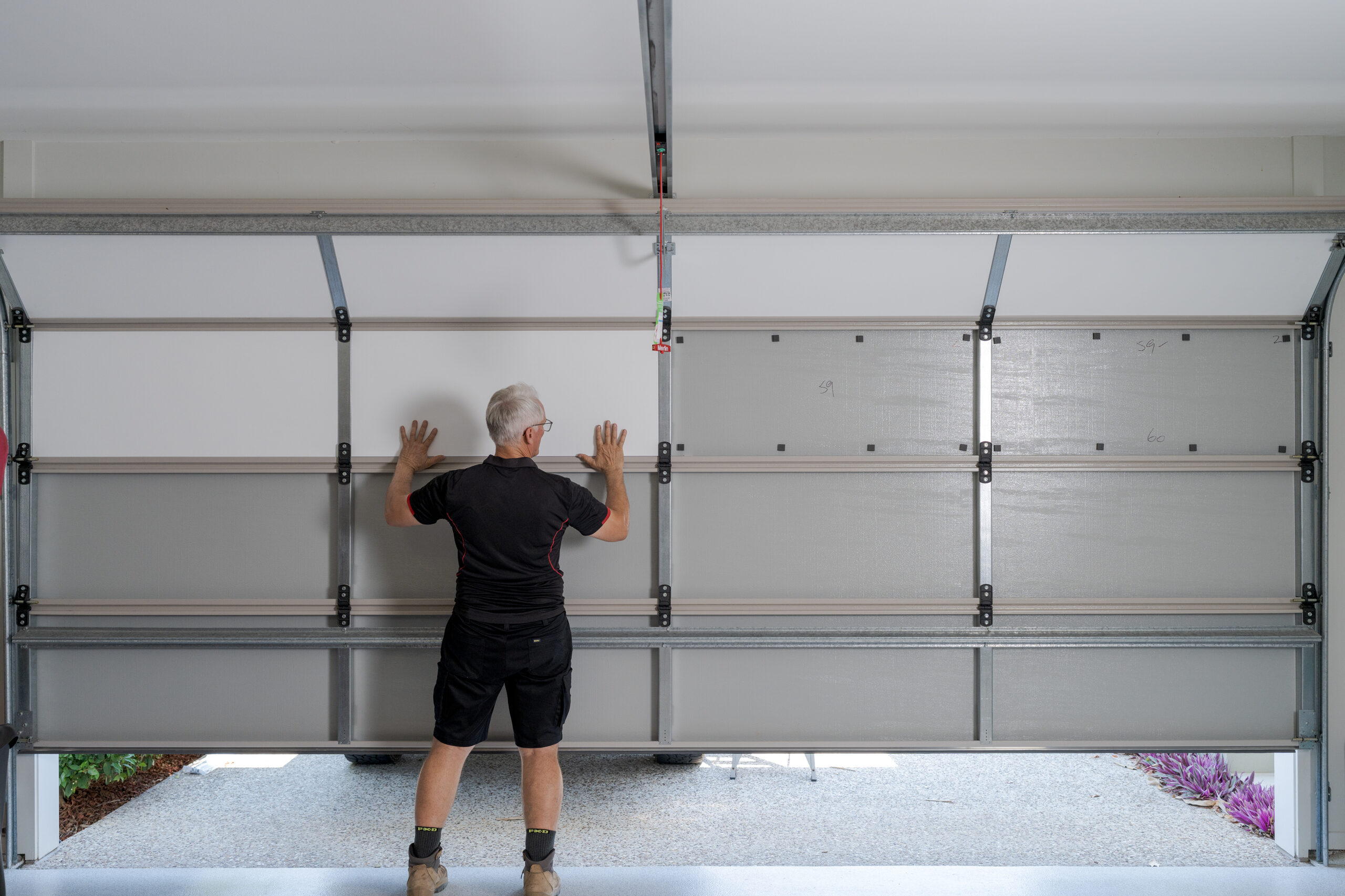 Installer fitting purpose-built garage door insulation panels to reduce summer heat and keep an Australian garage cool without air-conditioning